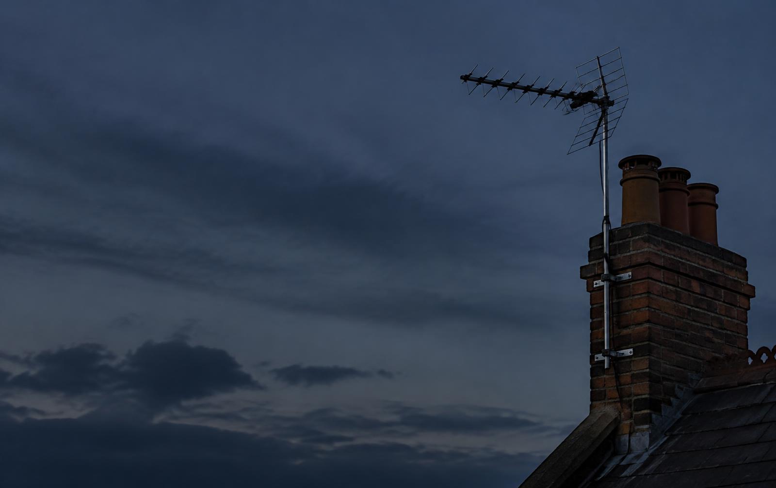 Illustrative image: TV aerial on a steel mast fixed to a brick chimney at dusk